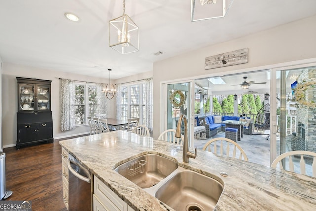 kitchen featuring light stone counters, a sink, dark wood-type flooring, stainless steel dishwasher, and decorative light fixtures