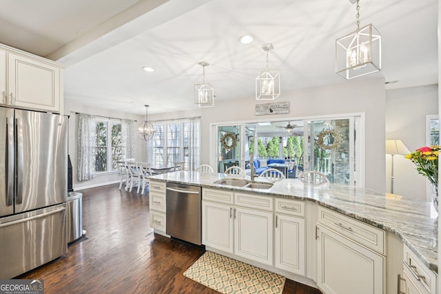 kitchen with ceiling fan with notable chandelier, a sink, light stone counters, stainless steel appliances, and dark wood-style flooring