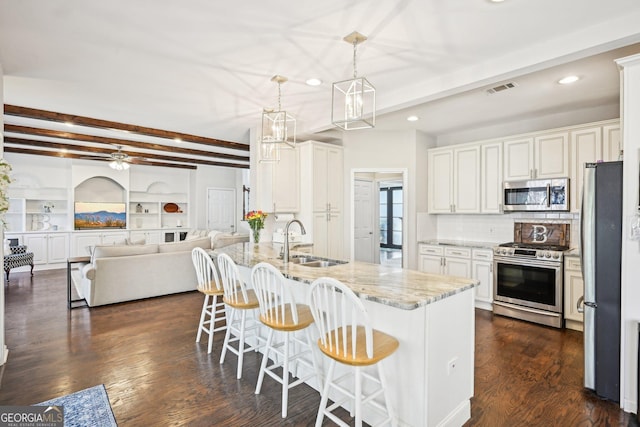 kitchen with visible vents, beam ceiling, a sink, stainless steel appliances, and light stone countertops