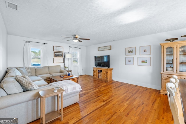 living room with visible vents, a textured ceiling, light wood finished floors, baseboards, and ceiling fan