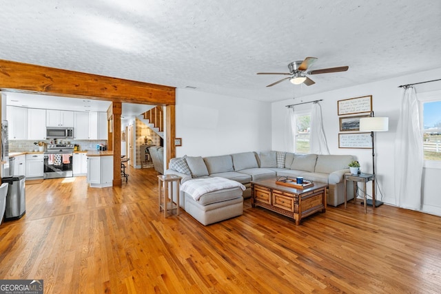 living area featuring a textured ceiling, ceiling fan, stairs, and light wood finished floors