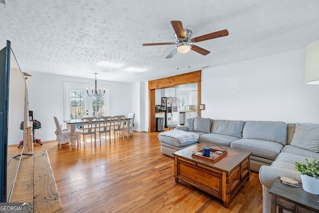 living area featuring light wood finished floors, ceiling fan with notable chandelier, and a textured ceiling