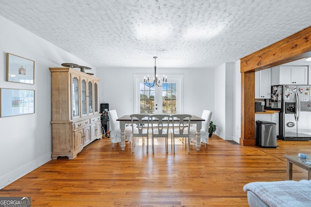 dining room featuring baseboards, a textured ceiling, a chandelier, and light wood finished floors