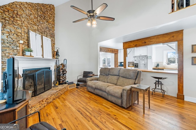 living room featuring a towering ceiling, a fireplace with raised hearth, a ceiling fan, and wood finished floors