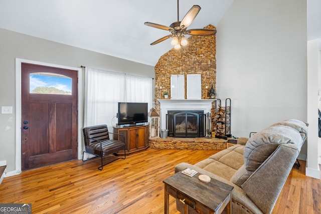 living room with light wood-style floors, a stone fireplace, ceiling fan, and high vaulted ceiling