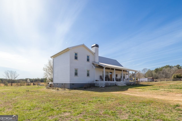 view of side of property featuring covered porch, a lawn, a chimney, and crawl space