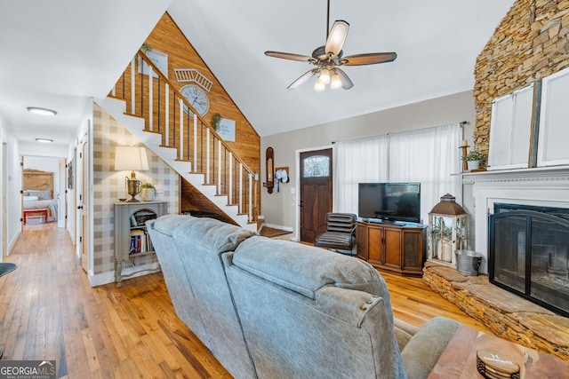 living area featuring high vaulted ceiling, a ceiling fan, a glass covered fireplace, light wood finished floors, and stairs