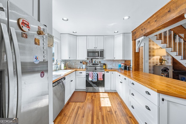 kitchen featuring a peninsula, a sink, stainless steel appliances, white cabinetry, and light wood-type flooring