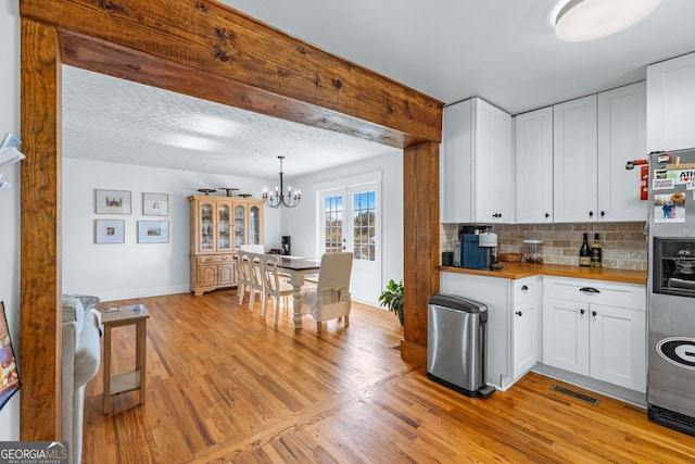 kitchen with visible vents, light wood-style floors, stainless steel refrigerator with ice dispenser, white cabinetry, and backsplash