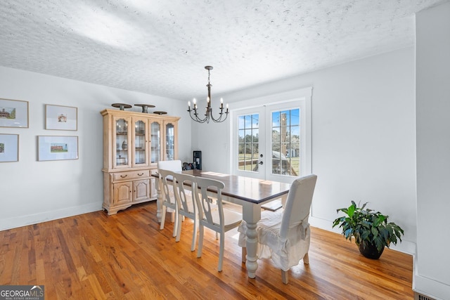 dining area with a textured ceiling, wood finished floors, french doors, an inviting chandelier, and baseboards