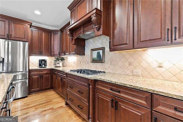 kitchen with light wood-style flooring, backsplash, light stone countertops, and appliances with stainless steel finishes