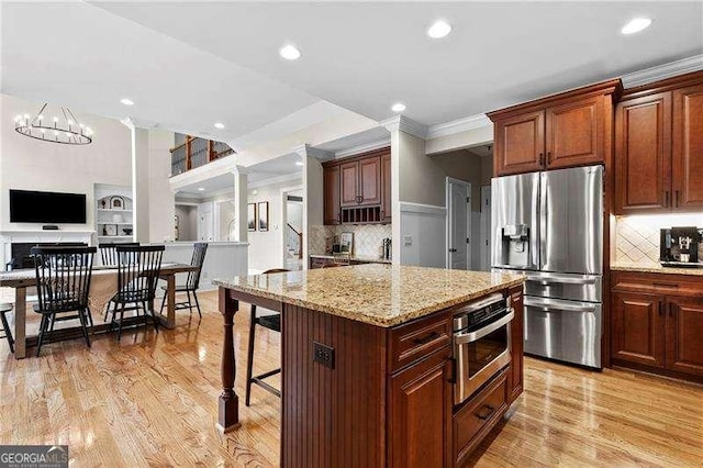 kitchen featuring light wood-style flooring, appliances with stainless steel finishes, ornamental molding, and ornate columns