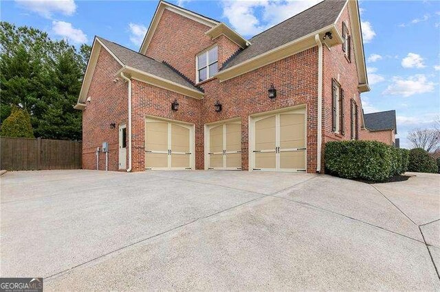 view of side of home with brick siding, driveway, and fence