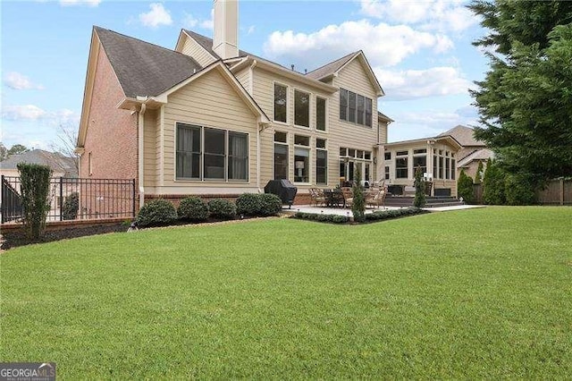 back of house featuring a patio, fence, a chimney, a lawn, and brick siding