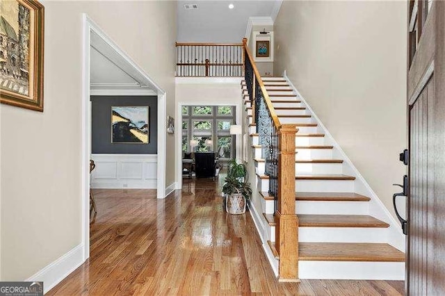 foyer entrance featuring ornamental molding, wood finished floors, baseboards, a towering ceiling, and stairs