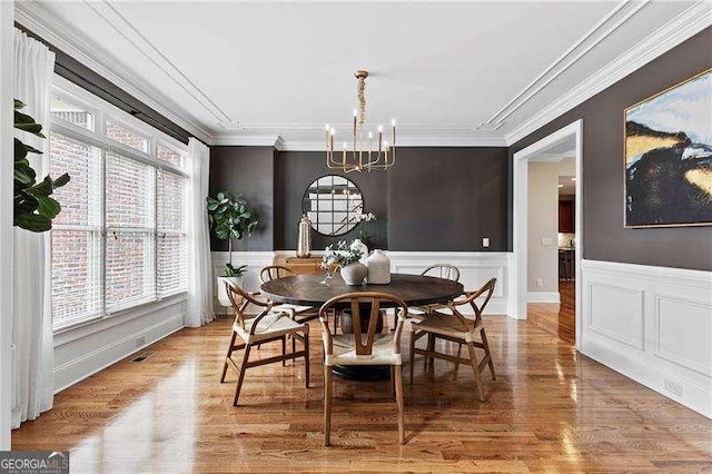 dining room featuring wood finished floors, visible vents, a wainscoted wall, crown molding, and a chandelier