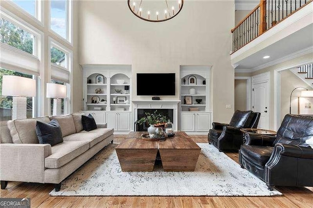 living room with built in shelves, crown molding, a lit fireplace, wood finished floors, and a notable chandelier