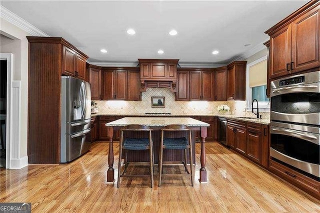 kitchen with ornamental molding, appliances with stainless steel finishes, light wood-type flooring, and a sink