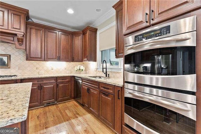 kitchen with backsplash, light stone countertops, light wood-style flooring, stainless steel appliances, and a sink