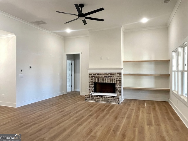 unfurnished living room with ornamental molding, wood finished floors, baseboards, a brick fireplace, and ceiling fan