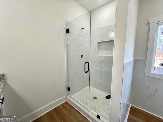 bathroom with a marble finish shower and wood finished floors