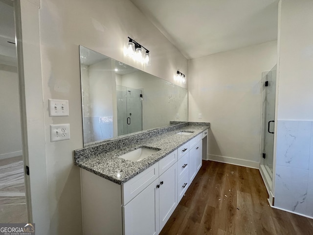 full bath featuring a sink, wood finished floors, a shower stall, double vanity, and baseboards