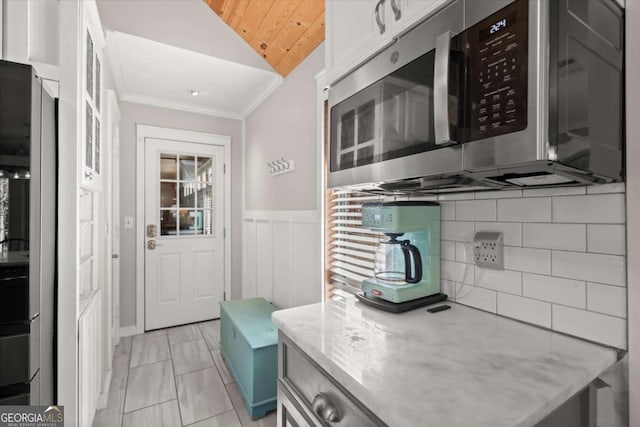 kitchen with a wainscoted wall, stainless steel microwave, white cabinets, crown molding, and lofted ceiling