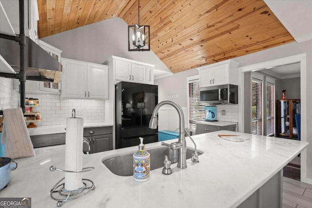 kitchen featuring a sink, stainless steel microwave, freestanding refrigerator, wooden ceiling, and light countertops