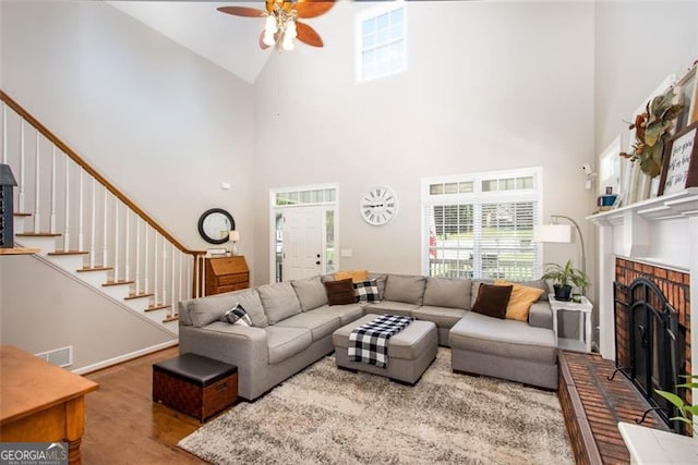 living room with stairway, wood finished floors, a fireplace, ceiling fan, and a towering ceiling