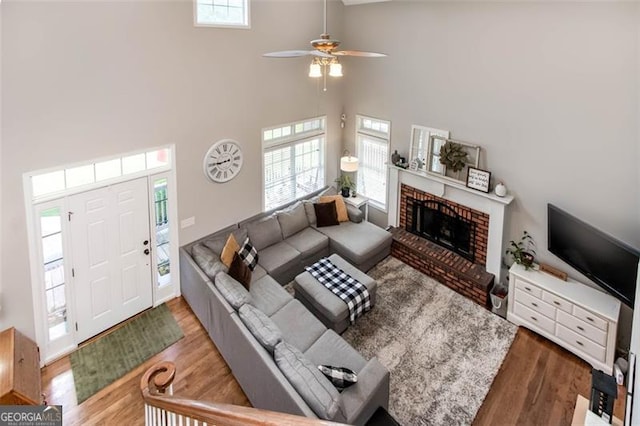 living area with plenty of natural light, a brick fireplace, wood finished floors, and a ceiling fan