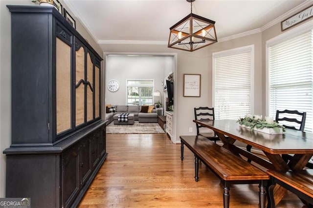 dining area with light wood-style floors, an inviting chandelier, and ornamental molding