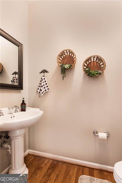 half bathroom featuring toilet, wood finished floors, baseboards, and a sink