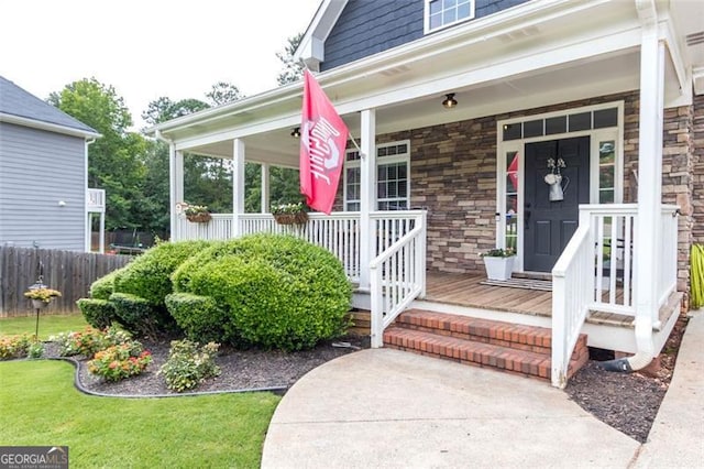 entrance to property with stone siding, a porch, and fence