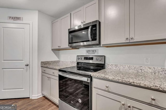 kitchen with light wood finished floors, light stone countertops, baseboards, and appliances with stainless steel finishes