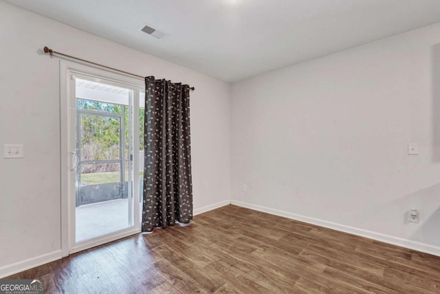 spare room with wood finished floors, visible vents, and baseboards