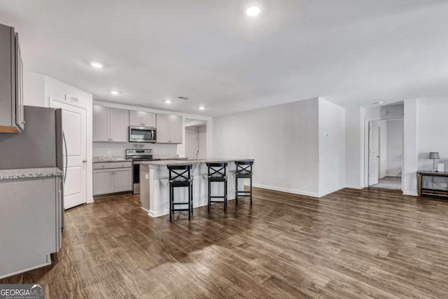 kitchen with a center island, gray cabinets, a kitchen breakfast bar, stainless steel appliances, and dark wood-style flooring