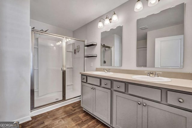 bathroom featuring a shower stall, wood finished floors, double vanity, and a sink