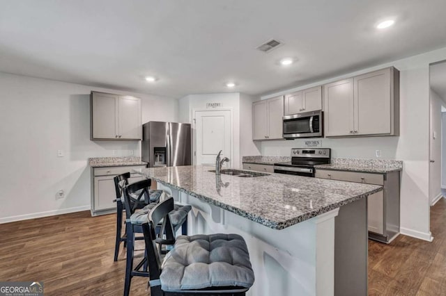 kitchen with a kitchen bar, light stone counters, gray cabinets, stainless steel appliances, and a sink