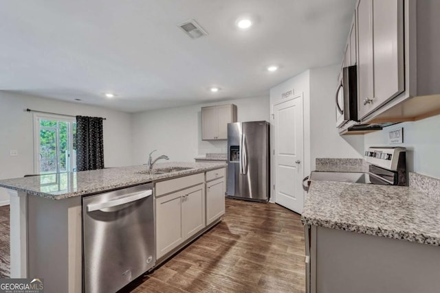 kitchen featuring visible vents, a sink, an island with sink, appliances with stainless steel finishes, and dark wood-style flooring