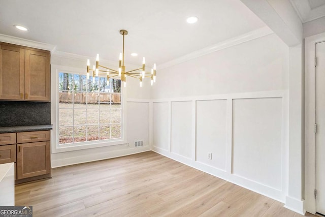 unfurnished dining area featuring an inviting chandelier, light wood-style flooring, recessed lighting, ornamental molding, and a decorative wall