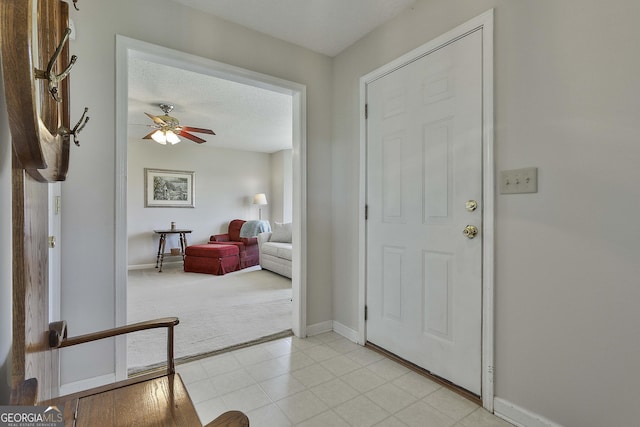 foyer entrance featuring baseboards, light colored carpet, light tile patterned flooring, a textured ceiling, and a ceiling fan