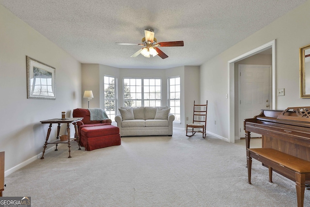 carpeted living area with baseboards, a textured ceiling, and a ceiling fan