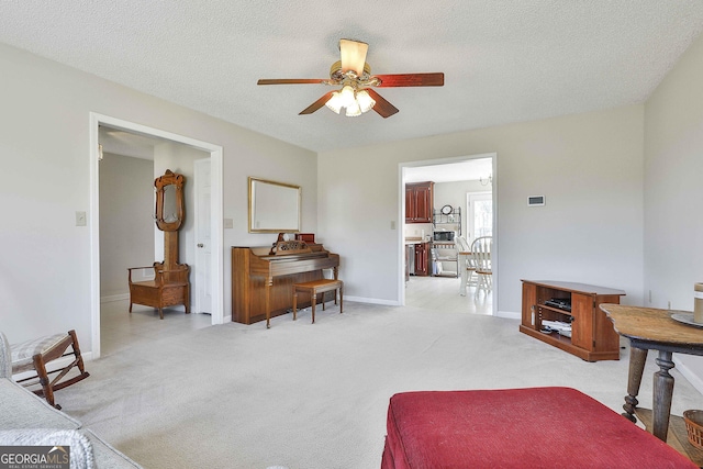 living room with ceiling fan, a textured ceiling, baseboards, and light carpet