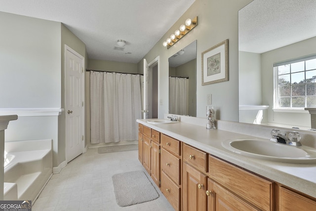 full bathroom featuring double vanity, a textured ceiling, a tub, and a sink