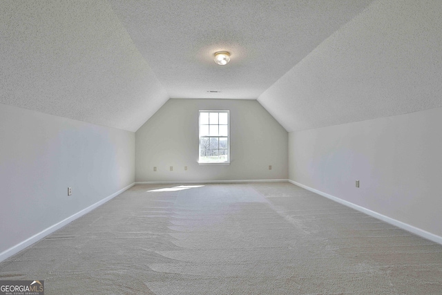 additional living space with a textured ceiling, baseboards, carpet, and vaulted ceiling