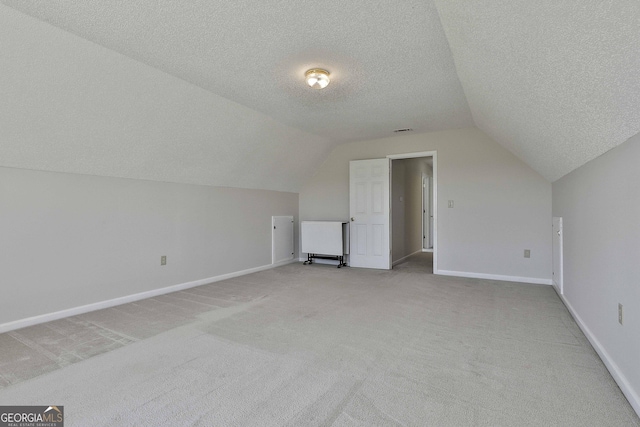 additional living space featuring visible vents, baseboards, vaulted ceiling, light carpet, and a textured ceiling