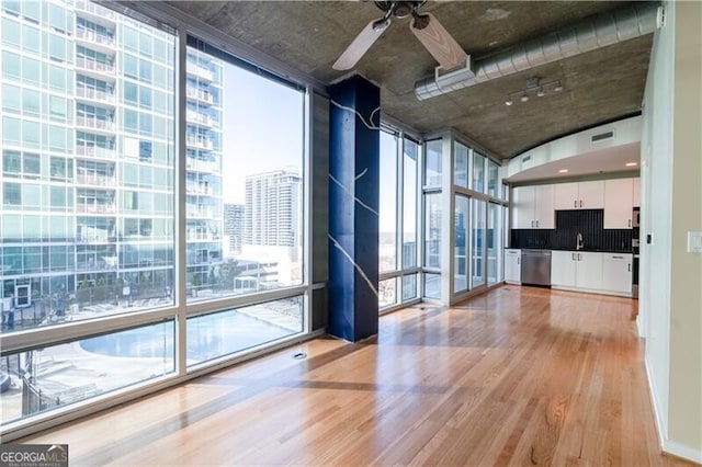 unfurnished living room with a ceiling fan, light wood finished floors, a sink, floor to ceiling windows, and a view of city