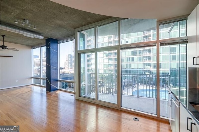 unfurnished room with floor to ceiling windows, ceiling fan, and wood finished floors