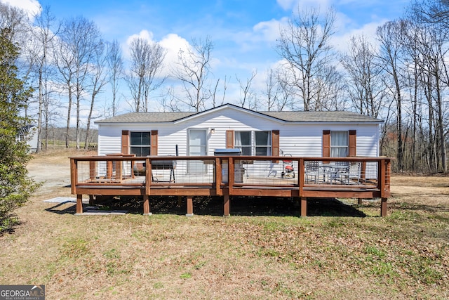 back of property featuring a yard, a deck, and roof with shingles