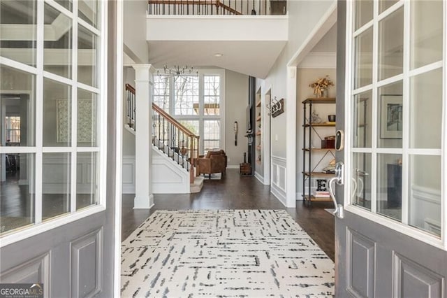 foyer entrance featuring stairway, a decorative wall, wood finished floors, and ornate columns